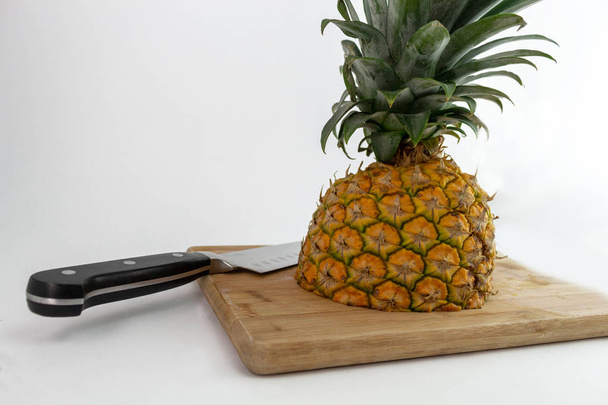 снимок трех четвертей ананаса, разрезанного на доске с ножом
 - Фото, изображение