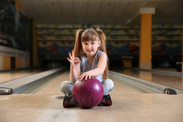 Mała dziewczynka z piłką pokazująca OK w Bowling Club - Zdjęcie, obraz
