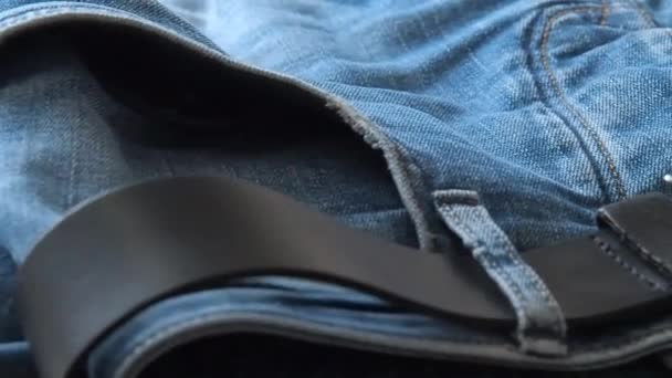 Blue jeans with leather belt laying on table, close shot. Blurred background. Selective soft focus. Camera moving along belt and front trouser pockets. Background for fashion banners and wallpapers. - Video, Çekim
