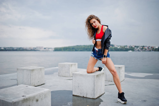 Sexy curly model girl in red top, jeans denim shorts, leather ja - Fotó, kép