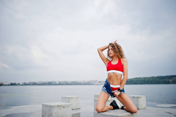 Sexy curly model girl in red top, jeans denim shorts and sneaker - Foto, Imagen