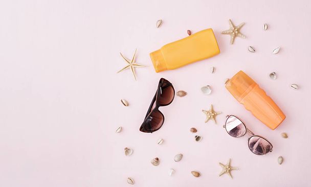 Sunglasses with sunscreen cream, defferent seashell and starfish on pink background. Top view. Flat lay - 写真・画像
