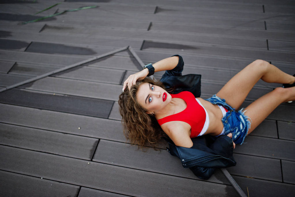 Sexy curly model girl in red top, jeans denim shorts, leather ja - 写真・画像