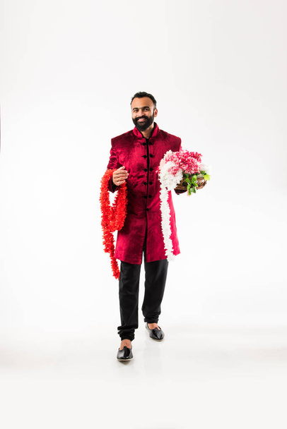 Indiase man Holding Flower Garland/serie voor decoratie op Diwali/bruiloft of festivals terwijl het dragen van traditionele doeken/Sherwani, staande geïsoleerd over witte achtergrond - Foto, afbeelding