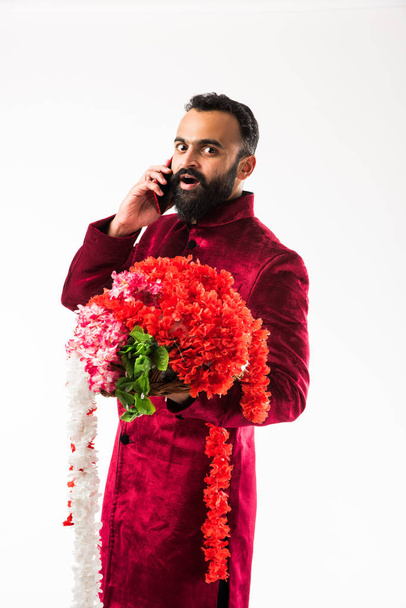Indian man holding flower garland / series for decoration on diwali/ wedding or festivals while wearing traditional cloths / sherwani , standing isolated over white background - Valokuva, kuva