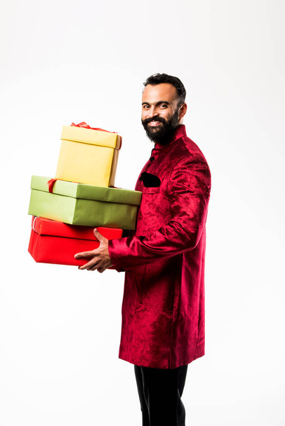 Индийский весёлый бородатый мужчина в традиционной одежде / шервани с подарочной коробкой на белом фоне
 - Фото, изображение