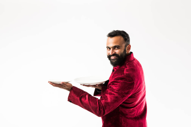 Indian Man holding empty plate while wearing traditional Sherwani on Diwali or wedding party, standing isolated over white background - Photo, Image