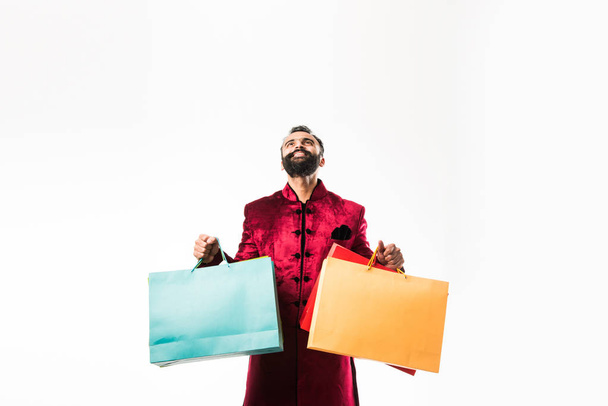 Indian Young man shopping while wearing red traditional wear, standing isolated over white background - Foto, immagini