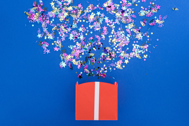 Vue du dessus de la boîte-cadeau avec des confettis lumineux brillants sur fond bleu
 - Photo, image