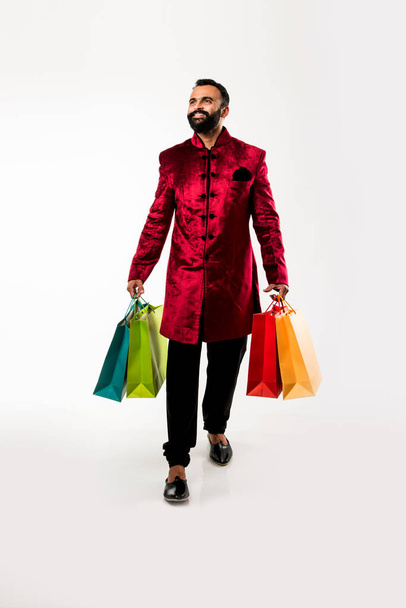 Indian Young man shopping while wearing red traditional wear, standing isolated over white background - Foto, Bild
