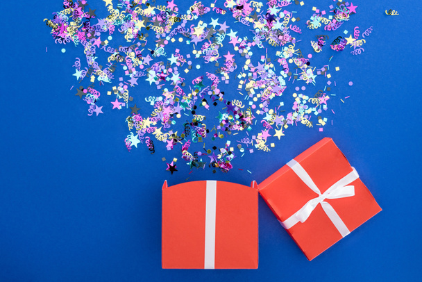 rode geschenk doos en veelkleurige glanzende confetti op blauwe achtergrond - Foto, afbeelding