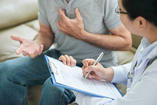 Bijgesneden beeld van arts praten met patiënt en vullen verzekeringsclaim formulier - Foto, afbeelding