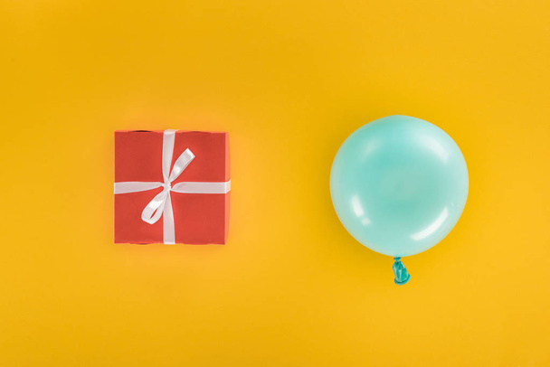 Top view of blue balloon and red gift box on yellow background - Foto, immagini