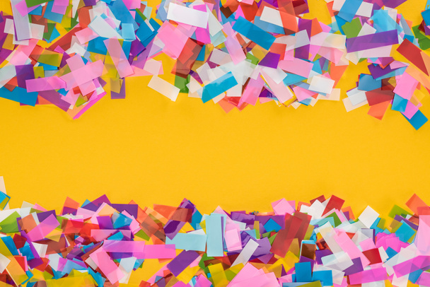 Top view of multicolored confetti frame on yellow background  - 写真・画像