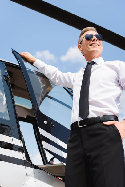 Piloto sonriente en ropa formal y gafas de sol abriendo la puerta del helicóptero
 - Foto, Imagen
