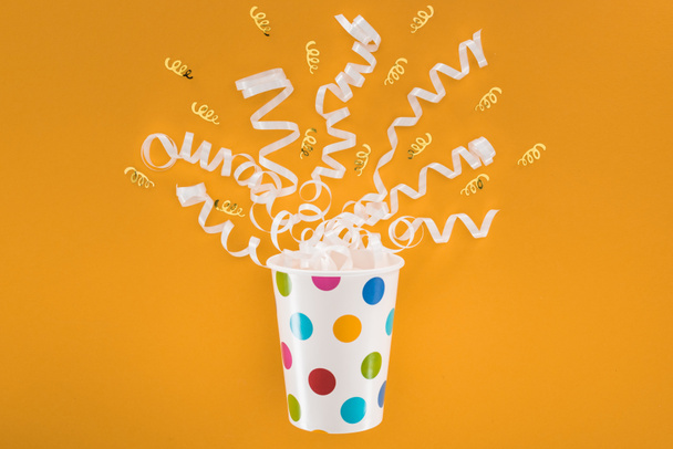 white and golden ribbons in polka dot cup on orange background - Foto, Bild
