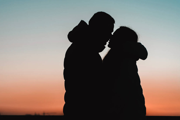 Silhouette of a lovely couple against the background of the lake and evening sky in the park. - 写真・画像