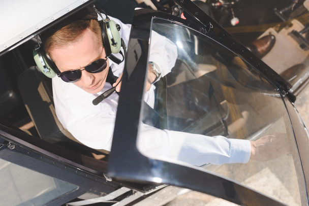felülnézet Pilot napszemüvegben és fülhallgatóval ülve helikopteres kabinban - Fotó, kép