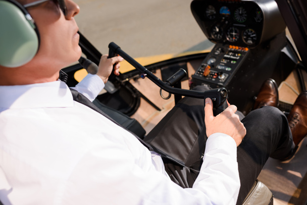 piloto maduro em desgaste formal sentado na cabine de helicóptero e roda de apoio
 - Foto, Imagem