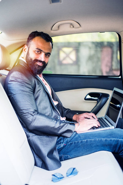 Indian/asian young businessman using laptop computer and phone inside the car, selective focus - Fotografie, Obrázek
