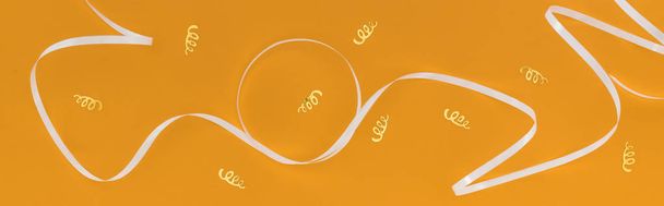 Panoramic shot of white ribbon and gold confetti on orange background - Photo, Image