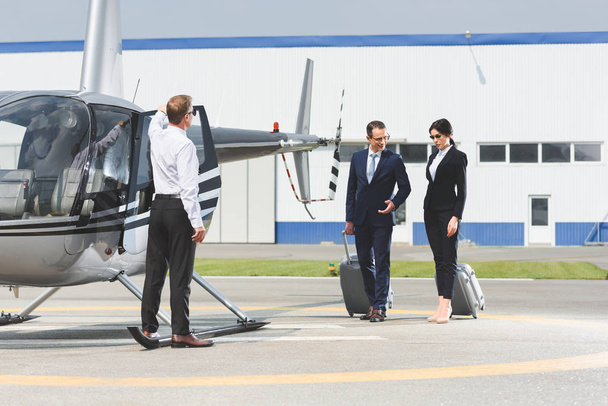 business partners in formal wear with suitcases near pilot and helicopter - Φωτογραφία, εικόνα