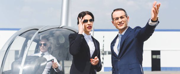 panoramic shot of businesspeople in suits Gesturing near helicopter with pilot - Photo, Image