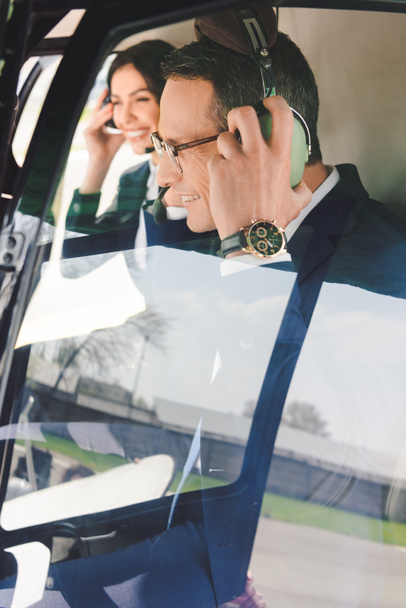 businesswoman and smiling businessman with headset sitting in helicopter cabin - Foto, afbeelding