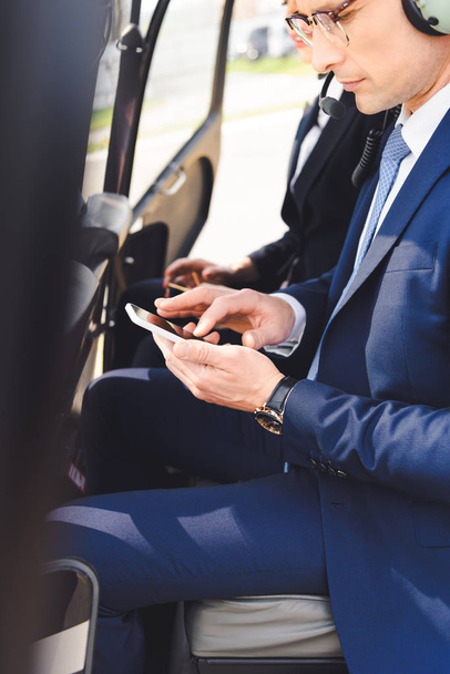 biznesmen w odzieży formalnej siedzącej w kabinie śmigłowca i za pomocą smartfona - Zdjęcie, obraz