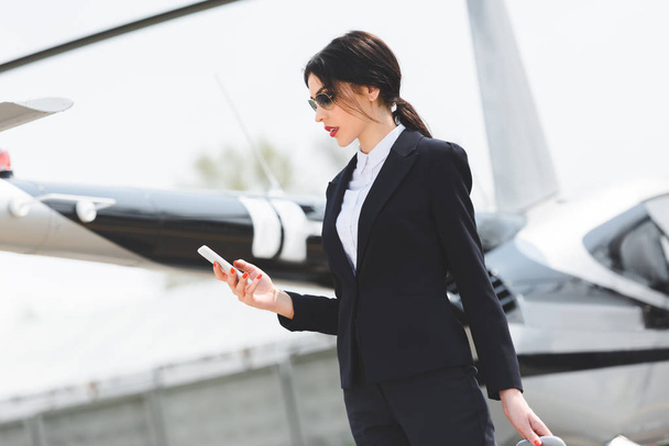 businesswoman in formal wear using smartphone near helicopter - Photo, Image