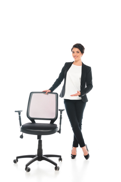 sonriente mixta mujer de negocios de pie cerca de la silla de oficina sobre fondo blanco
 - Foto, imagen