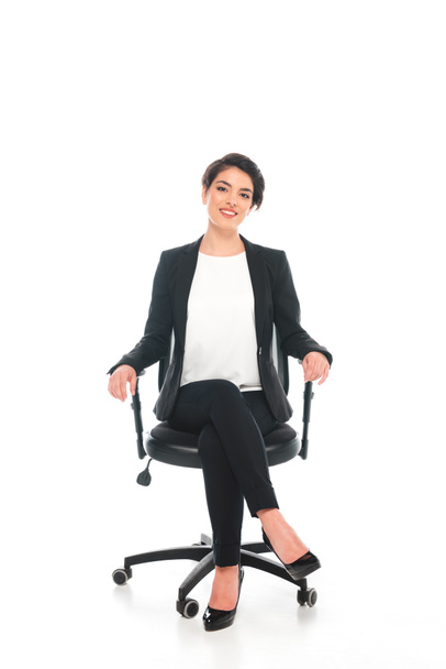 smiling mixed race businesswoman sitting in office chair and smiling at camera on white background - Valokuva, kuva