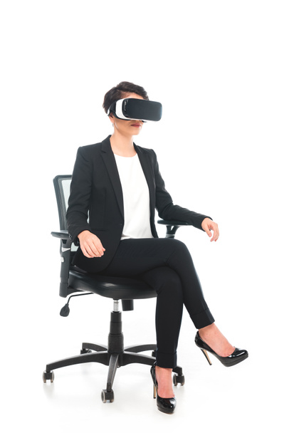mixed race zakenvrouw met behulp van Virtual Reality headset zittend in bureaustoel op witte achtergrond - Foto, afbeelding