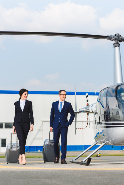 businessman and businesswoman with suitcases near helicopter - Фото, изображение