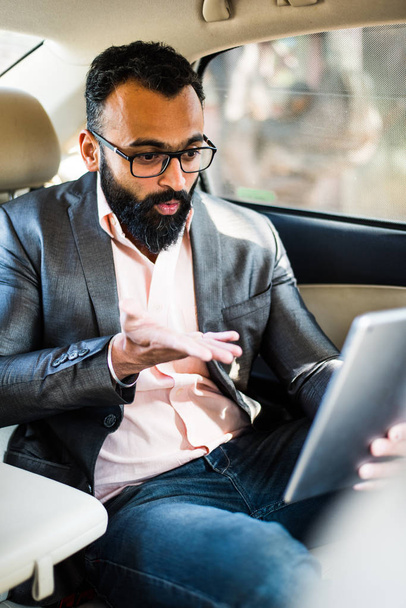 Indien / asiatique jeune homme d'affaires en utilisant Tablette ordinateur / onglet tandis que assis sur le siège arrière, mise au point sélective
 - Photo, image