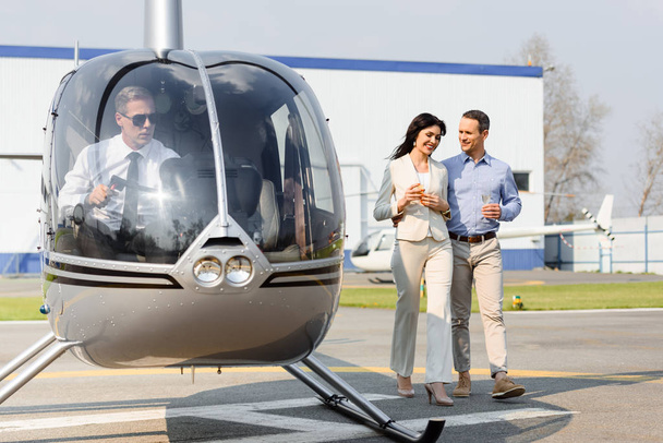 husband and wife with champagne glasses on romantic date near helicopter - Foto, imagen