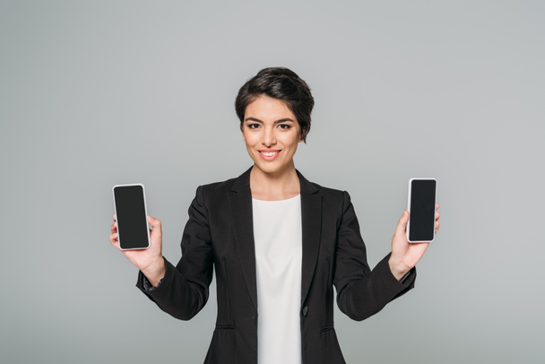 Veselý smíšený závod, obchodní žena zobrazující telefony Smartphone s prázdnou obrazovkou izolovaná na šedé - Fotografie, Obrázek