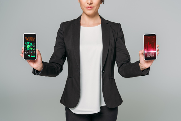 gri izole ekranda ticaret kursları ve pazarlama analizi uygulamaları ile akıllı telefonlar tutan karışık ırk iş kadını kısmi görünümü - Fotoğraf, Görsel