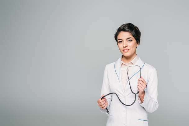 pretty mixed race doctor with stethoscope looking at camera isolated on grey - Zdjęcie, obraz
