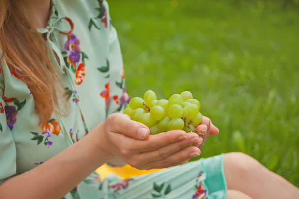 Woman sitting on the yellow cover and holding bunch of grapes. - Foto, afbeelding