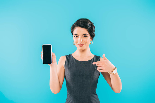 smiling mixed race woman pointing with finger at smartphone with blank screen isolated on blue - Fotó, kép