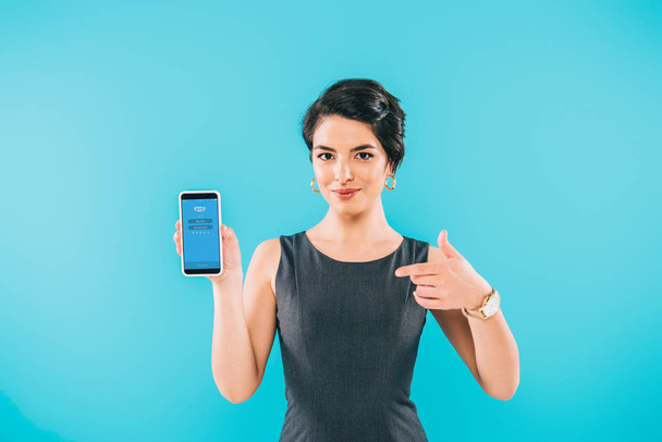 キエフ、 ウクライナ - 2019年4月24日:青で隔離された画面上のSkypeアプリでスマートフォンを示すかなり混合レースの女性. - 写真・画像