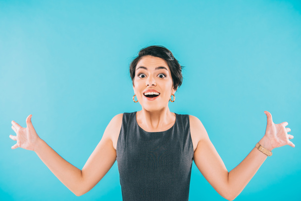 excited mixed race woman gesturing while looking at camera isolated on blue - Foto, Imagen