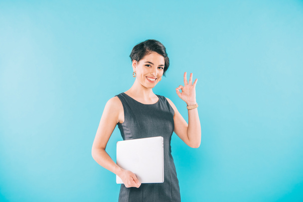 souriant mixte femme d'affaires tenant un ordinateur portable et agitant la main tout en regardant la caméra sur fond bleu
 - Photo, image