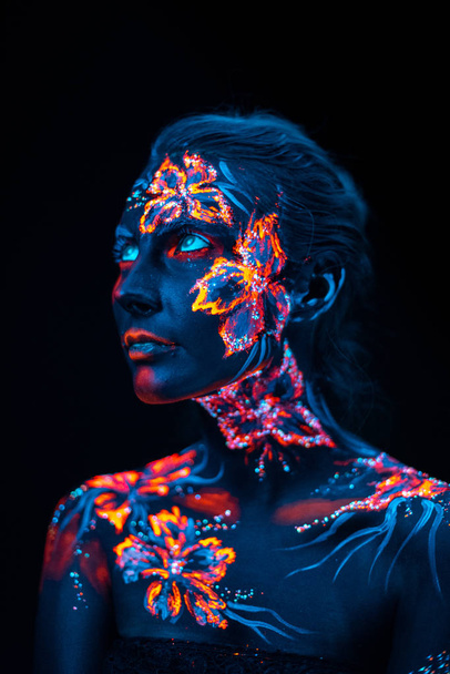 schöne Blumen im UV-Licht auf Gesicht und Körper eines jungen Mädchens - Foto, Bild