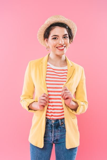 attractive mixed race woman in bright clothing and straw hat smiling at camera isolated on pink - Foto, Imagen
