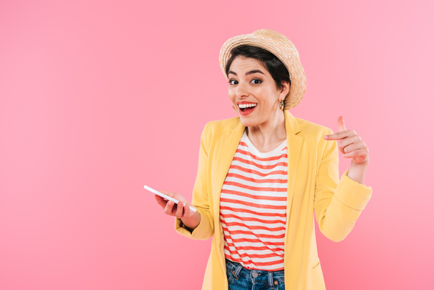 smiling mixed race woman pointing with finger at smartphone isolated on pink - Fotoğraf, Görsel