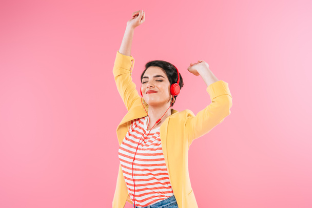 excited mixed race woman listening music in headphones and dancing isolated on pink - Photo, Image