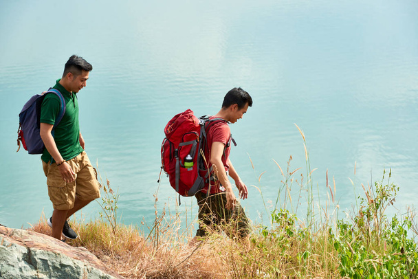 Dwa wędrowców z plecaki spaceru wzdłuż jeziora w poszukiwaniu najlepszego miejsca dla namiotu - Zdjęcie, obraz