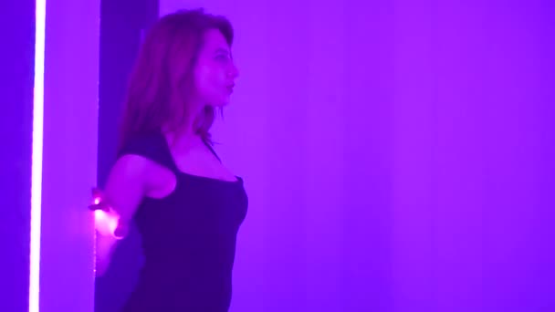 Joven mujer hermosa en vestido de cóctel negro bailando cerca del espejo con lámparas de neón. Club moda misterio joven beatiful chica sonriendo y seduciendo
 - Metraje, vídeo
